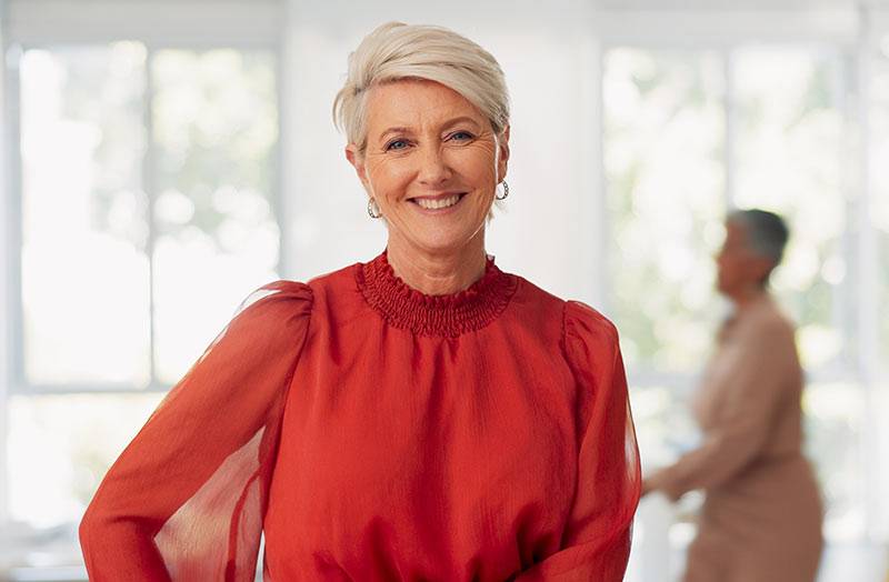 A smiling woman in her 60s standing indoors